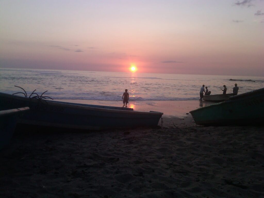 Sunset on a Nosara beach with fishing boats and silhouettes. Arrive with a reliable Nosara shuttle service.