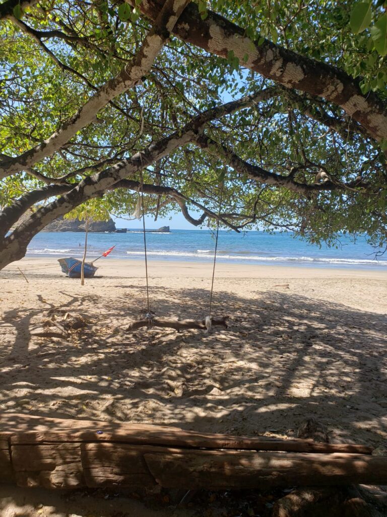 Shaded Nosara beach with tree swings and a fishing boat. Arrive with a reliable Nosara shuttle service.